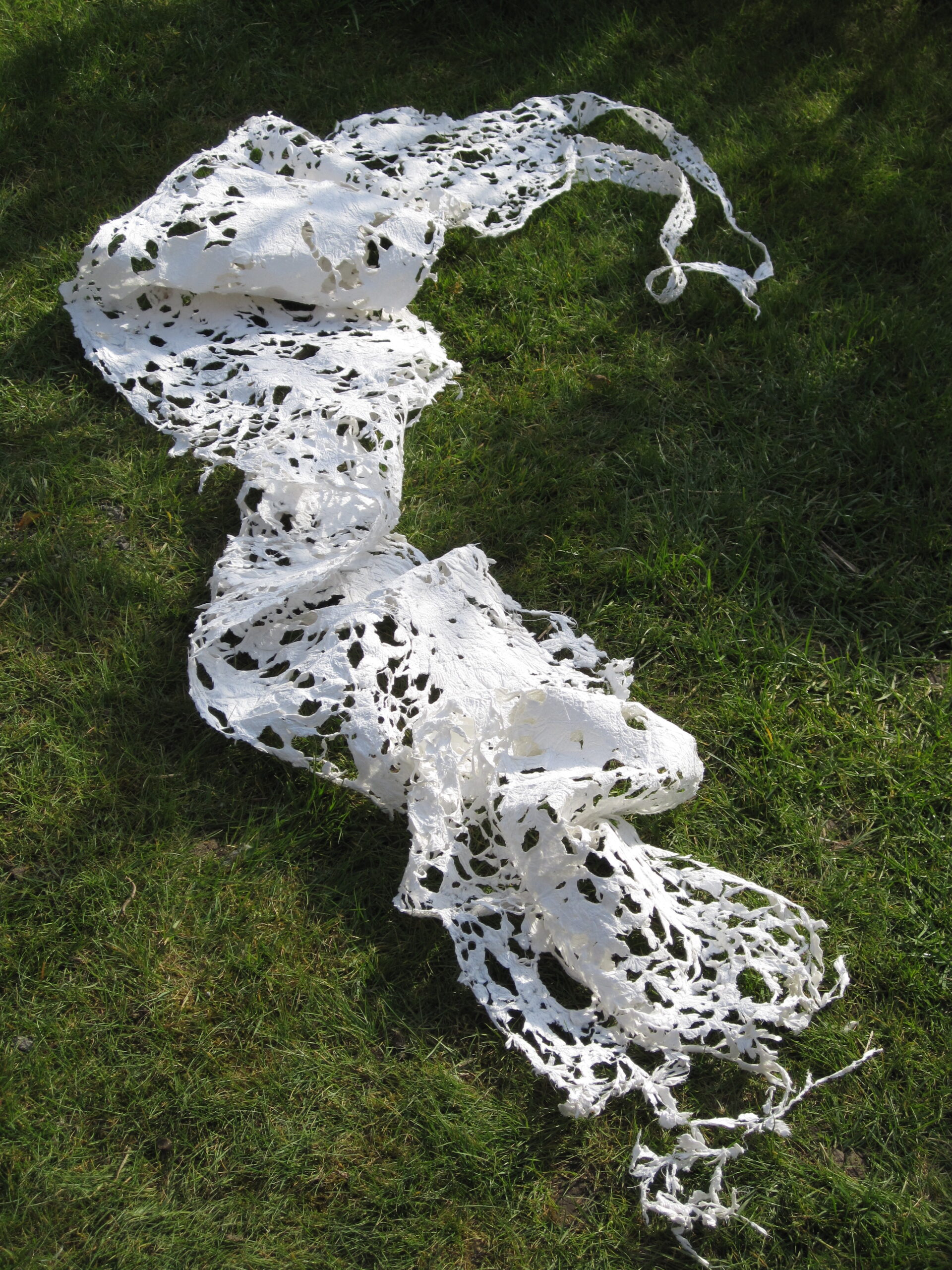 Delicate white paper-lace dress forms laid on green grass